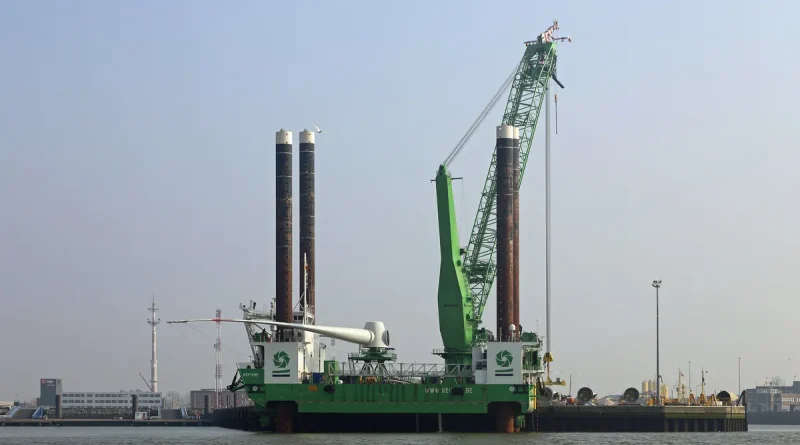 A jack-up rig with tall legs and a green crane standing in calm water