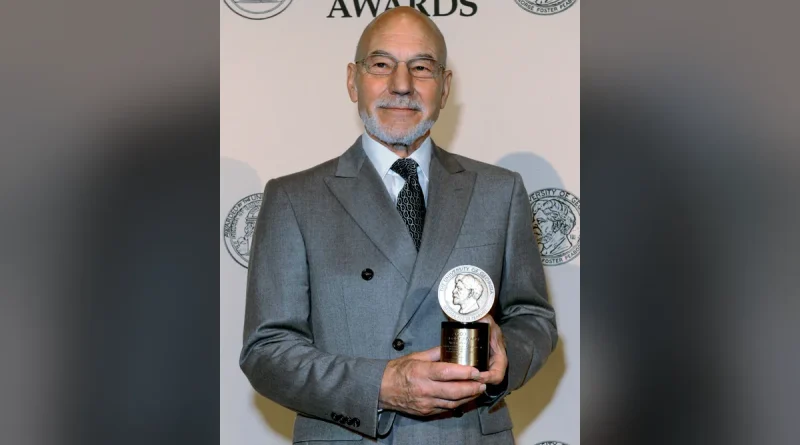 Sir Patrick Stewart smiling in a grey suit while holding a Peabody Award in 2012